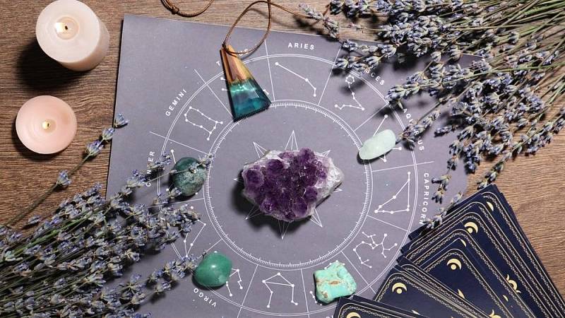 Astrologická předpověď. Kolo zvěrokruhu, drahokamy, tarotové karty a hořící svíčky na dřevěném stole.